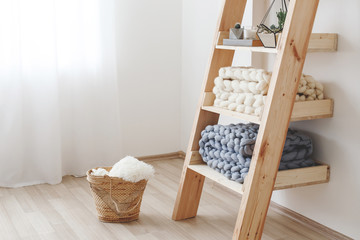 Fototapeta na wymiar Beige and grey knitted woolen merino plaid on wooden rack. Blanket of thick yarn. Chunky knit. Light stylish cozy scandinavian home interior decor.