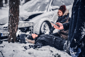 The witness of the accident keeps the phone and is going to call the rescue service. The car got into a skid and crashed into a tree on a snowy road. 