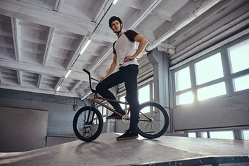 Teenage BMX rider standing with his bike getting ready to jump in a skatepark indoors