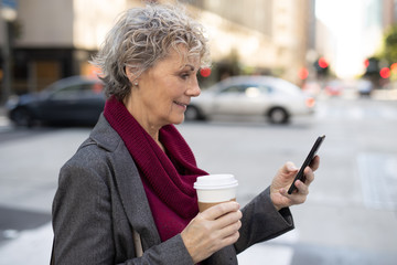Mature woman in city walking texting on cell phone