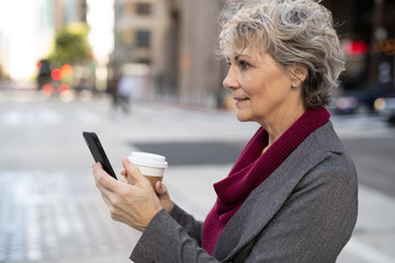 Mature woman in city walking texting on cell phone