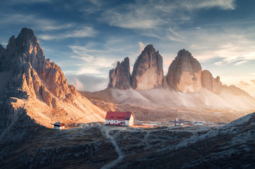 Mountain valley with beautiful house and church at sunset in autumn. Landscape with buildings, high rocks, trail, blue sky and sunlight. Mountains in Tre Cime park in Dolomites, Italy. Italian alps  - obrazy, fototapety, plakaty