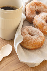 Sugar coated doughnuts on crumpled paper with a reusable cup of coffee , on wooden background.