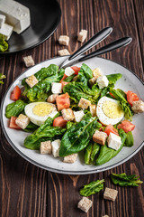 Fresh vegetable salad with tomatoes, spinach, bread crumbs, egg and feta. Healthy food. Dietary dinner or lunch menu. Salad plate on the table.