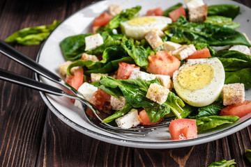 Fresh vegetable salad with tomatoes, spinach, bread crumbs, egg and feta. Healthy food. Dietary dinner or lunch menu. Salad plate on the table.