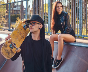 Stylish young couple in the skatepark at the summertime. Portrait of a skateboard in a hoodie and...