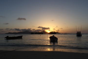 Fototapeta na wymiar Tropical sunset at beach. Anchored boats in the ocean and the Island of Praslin.