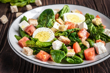 Fresh vegetable salad with tomatoes, spinach, bread crumbs, egg and feta. Healthy food. Dietary dinner or lunch menu. Salad plate on the table.