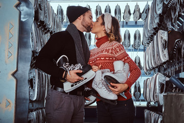 Young attractive couple in love, kiss while standing near rack with many pairs of skates