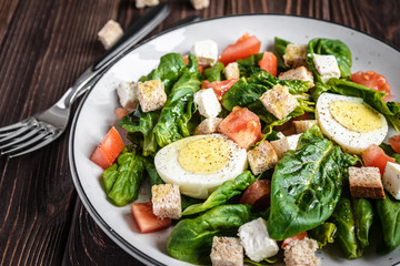 Fresh vegetable salad with tomatoes, spinach, bread crumbs, egg and feta. Healthy food. Dietary dinner or lunch menu. Salad plate on the table.