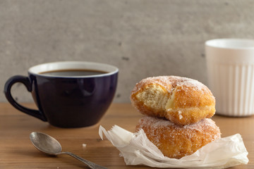Sugar coated doughnuts on crumpled paper with a two cups of coffee , on wooden tabletop.