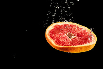 Grapefruit dropped into the water surrounded by bubbles