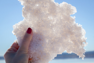 Female hand holding natural salt crystals on the background of a salt lake, side view close up
