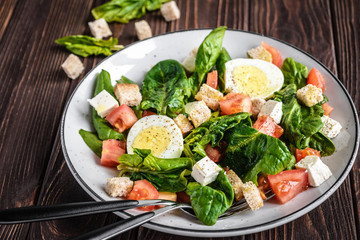 Fresh vegetable salad with tomatoes, spinach, bread crumbs, egg and feta. Healthy food. Dietary dinner or lunch menu. Salad plate on the table.