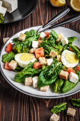 Fresh vegetable salad with tomatoes, spinach, bread crumbs, egg and feta. Healthy food. Dietary dinner or lunch menu. Salad plate on the table.