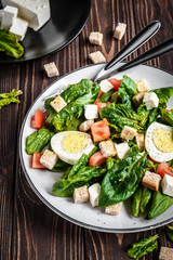 Fresh vegetable salad with tomatoes, spinach, bread crumbs, egg and feta. Healthy food. Dietary dinner or lunch menu. Salad plate on the table.