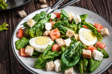 Fresh vegetable salad with tomatoes, spinach, bread crumbs, egg and feta. Healthy food. Dietary dinner or lunch menu. Salad plate on the table.