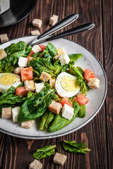 Fresh vegetable salad with tomatoes, spinach, bread crumbs, egg and feta. Healthy food. Dietary dinner or lunch menu. Salad plate on the table.
