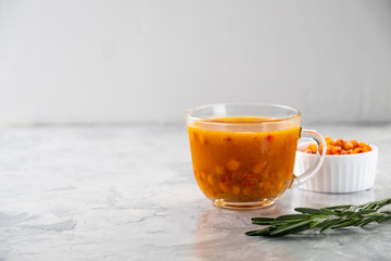 Colorful hot sea buckthorn tea with rosemary and fresh sea buckthorn berries on a grey table. Vitamin drink.