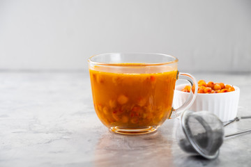 Colorful hot sea buckthorn tea with rosemary and fresh sea buckthorn berries on a grey table. Vitamin drink.