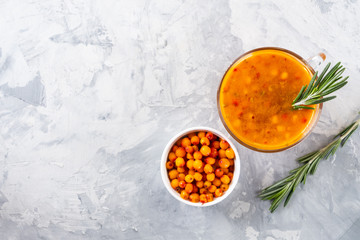 Colorful hot sea buckthorn tea with rosemary and fresh sea buckthorn berries on a grey table. Vitamin drink.
