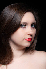Fototapeta premium Beautiful gray-eyed brown-haired woman with red lips and bared shoulders against black background. Closeup studio portrait