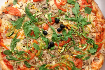 Large vegetarian pizza with tomato sauce, cheese, arugula, mushrooms, peppers and black olives. Top view. 