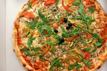 Large vegetarian pizza with tomato sauce, cheese, arugula, mushrooms, peppers and black olives. Top view. 