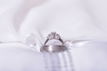 close up shot of male and female silver wedding rings joined together with a white wedding dress as the backdrop 