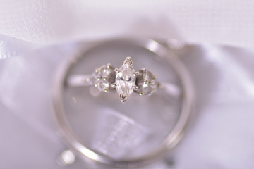 closeup macro shot of a diamond wedding ring standing up inside another wedding ring against a white wedding dress backdrop from overhead