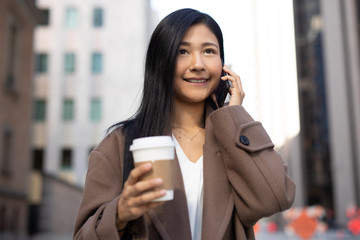 Young Asian woman in city walking talking on cell phone