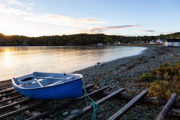 Fototapeta na wymiar Wooden boat laying by the Atlantic Ocean Shore during a vibrant sunrise. Taken in Beachside, Newfoundland, Canada.