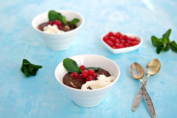 Sweet dessert, chocolate pudding in white portioned saucers on a light blue background. Served with whipped cream and red currant berries. Valentine's Day concept.
