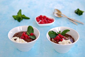 Sweet dessert, chocolate pudding in white portioned saucers on a light blue background. Served with whipped cream and red currant berries. Valentine's Day concept.
