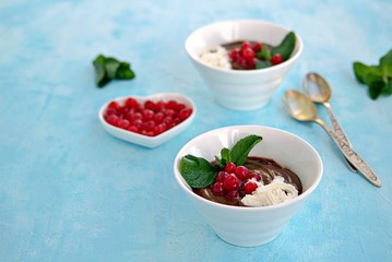 Sweet dessert, chocolate pudding in white portioned saucers on a light blue background. Served with whipped cream and red currant berries. Valentine's Day concept.