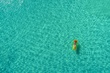 Aerial view of slim woman swimming on the swim mattress in the transparent turquoise sea in Seychelles. Summer seascape with girl, beautiful waves, colorful water. Top view from drone