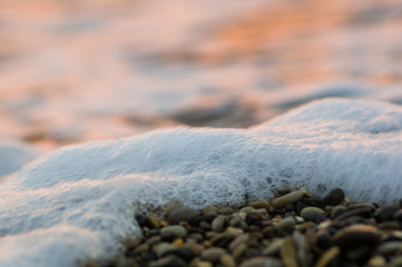 pebble stones on the sea beach, the rolling waves of the sea with foam