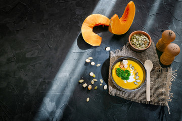 Homemade pumpkin soup in ceramic bowl with seeds, sour cream and bread croutons on dark background. Top view with copy space