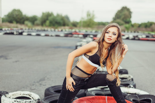 Gorgeous beauty model posing outdoors in street racing  with tires and cars on background. Speed, sport, beauty concept