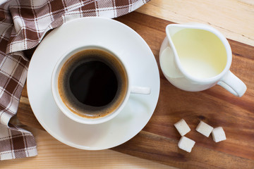 morning coffee in a white cup with lump sugar and milk on a wooden background
