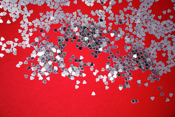 Valentine's Day. Lovers. Textures of silver sequins (paillettes) on a red background. Top view. Small hearts with a reflecting and mirrored surface, producing lights, glows, reflections, glitter
