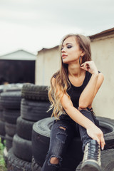 Gorgeous beauty model posing outdoors in street racing  with tires and cars on background. Speed, sport, beauty concept