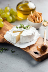 Brie cheese or camembert on cheese platter with crackers, grapes, olive oil. Closeup view, selective focus