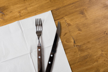 Cutlery and paper napkin on wooden background.