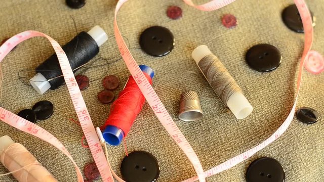 Accessories for sewing: needles, threads, buttons, a thimble and a tape measure on grungy background
