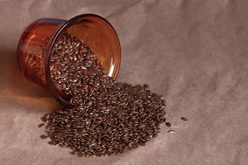Flax seeds in an inverted glass cup, scattered on the table, close-up on a paper background