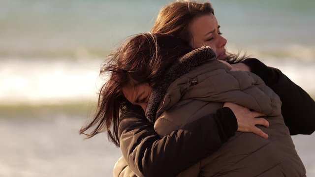 Two women hugging each other strong at sunset in front of the ocean slow motion