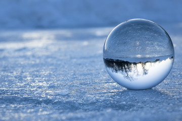 Blue reflection of the landscape in a glass sphere on the background of ice