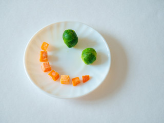 Smile face from vegetables on a white plate on a white background