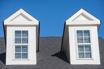 Double white dormer sash window with blue sky background on a gable roof with vinyl siding on a luxury estate house in the East Coast of the USA for upper middle class families